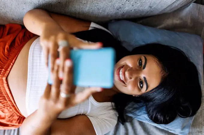 Smiling mid adult woman using smart phone while lying on sofa