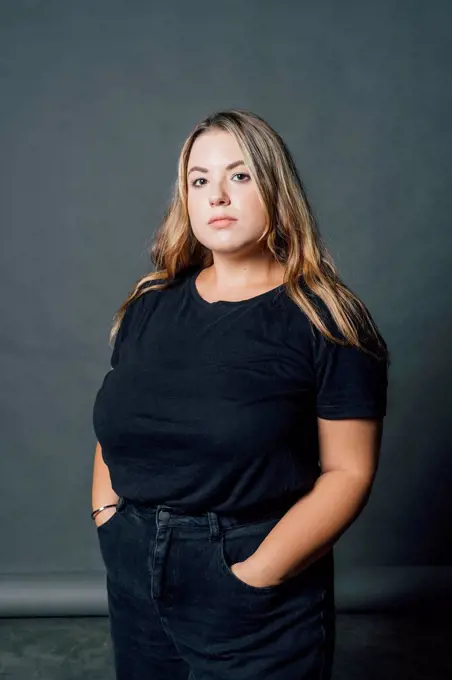 Confident voluptuous woman standing with hand in pockets at studio