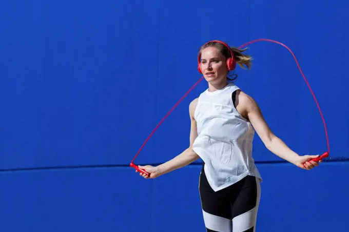 Female athlete jumping rope in front of blue wall