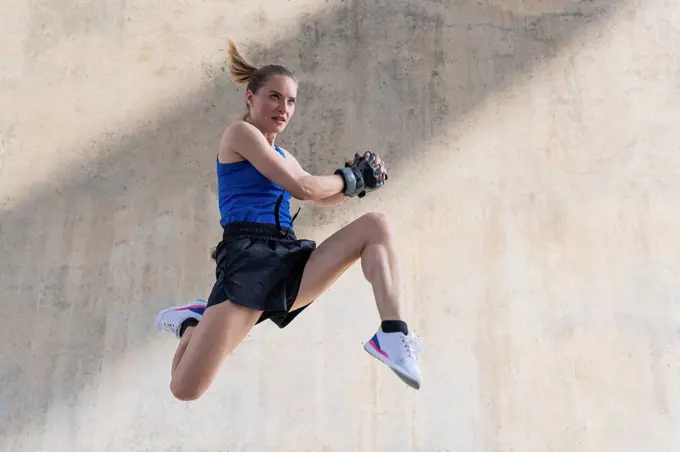 Determined female athlete jumping while exercising in front of wall