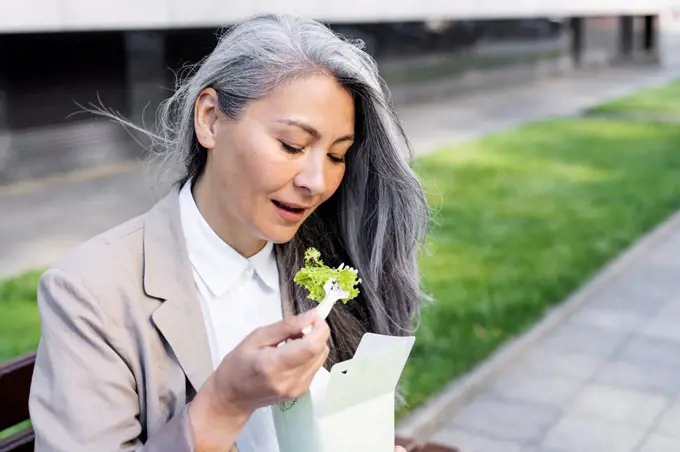 Mature woman eating salad from food box