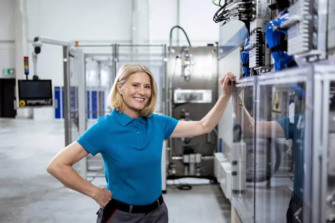 Smiling female professional with hand on hip standing by machinery in factory