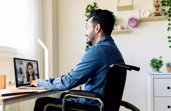 Smiling businessman talking with businesswoman on video conference through laptop at home