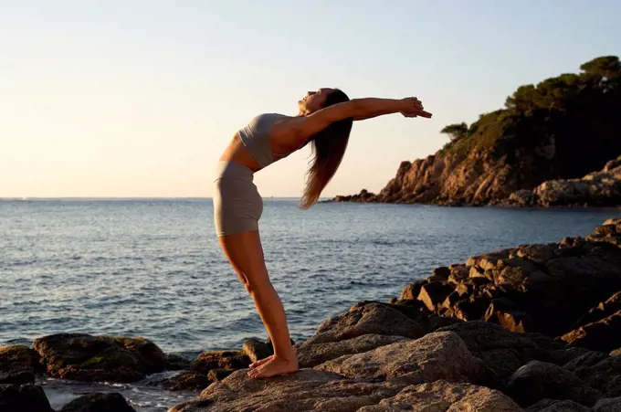 Flexible sportswoman practicing yoga on rock