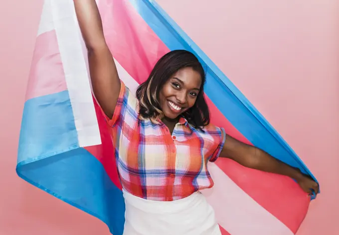 Happy woman holding transgender flag against pink background