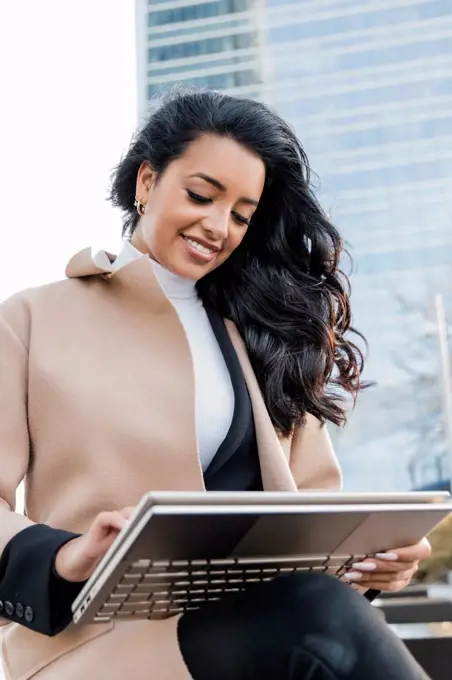 Smiling freelancer with long black hair using laptop