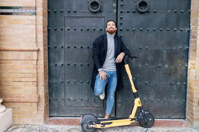 Young man with e-push scooter leaning on closed door