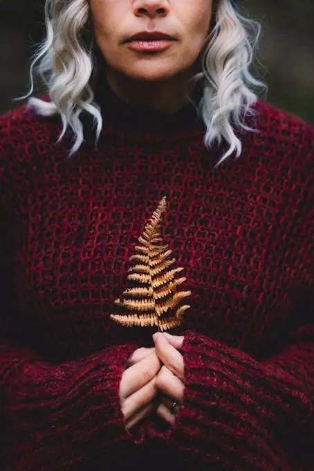 Woman wearing sweater holding dry leaf in forest