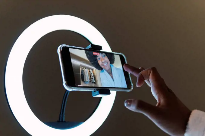 Smiling woman vlogging on smart phone in illuminated ring light