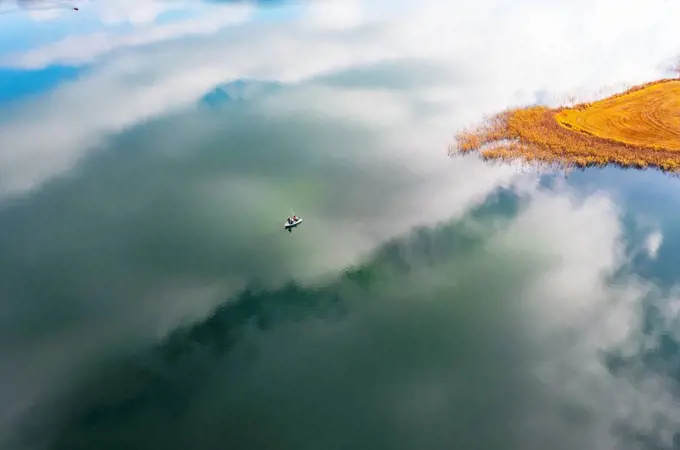 Drone view of clouds reflecting in Irrsee lake with lone fishing boat in center