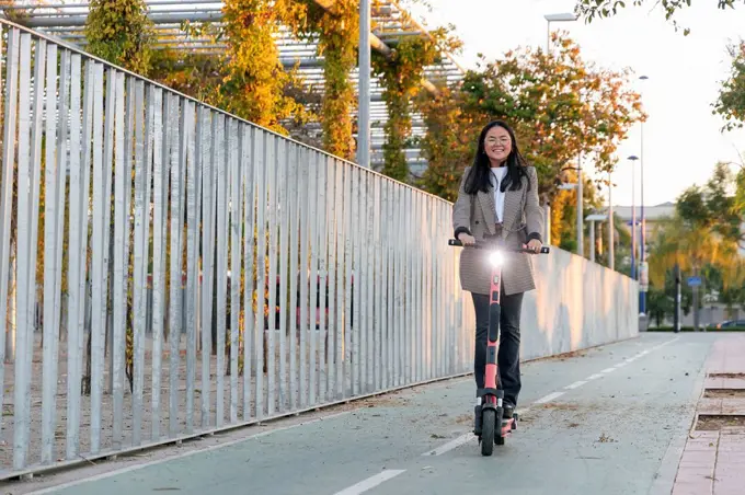 Businesswoman riding electric push scooter by fence on footpath