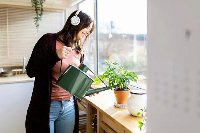 Woman listening music watering houseplant through can at home