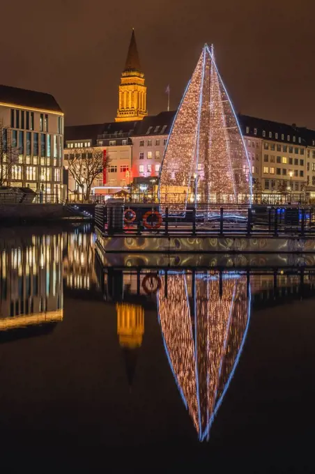 Germany, Schleswig-Holstein, Kiel, Large Christmas tree reflecting in city canal at night