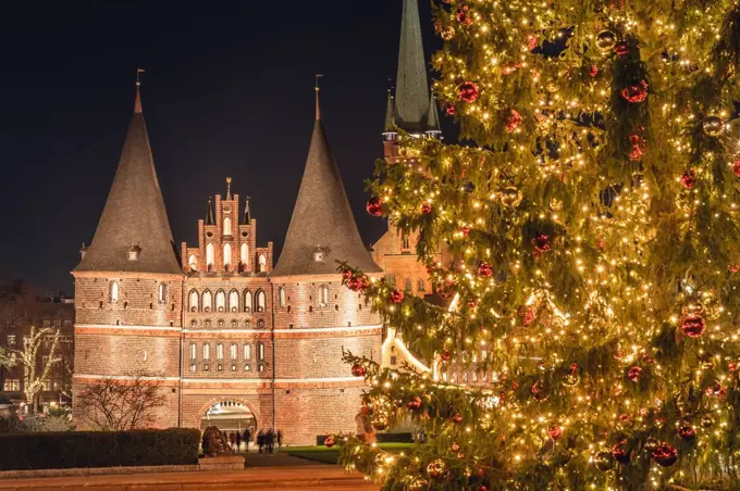 Germany, Schleswig-Holstein, Lubeck, Illuminated¶ÿHolstentor gate at night with glowing Christmas tree in foreground