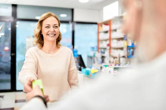 Smiling customer receiving medicine from pharmacist at pharmacy store