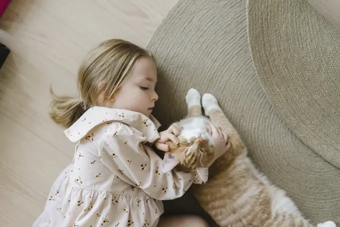 Blond girl stroking cat lying on floor at home