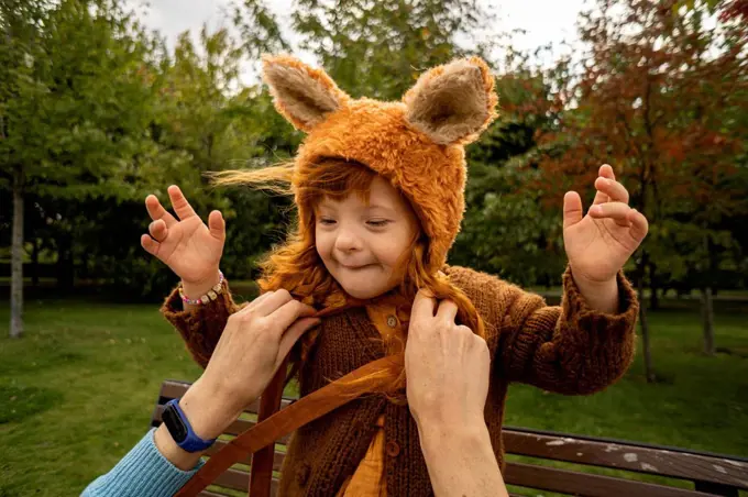 Mother tying bear costume hat of daughter at park