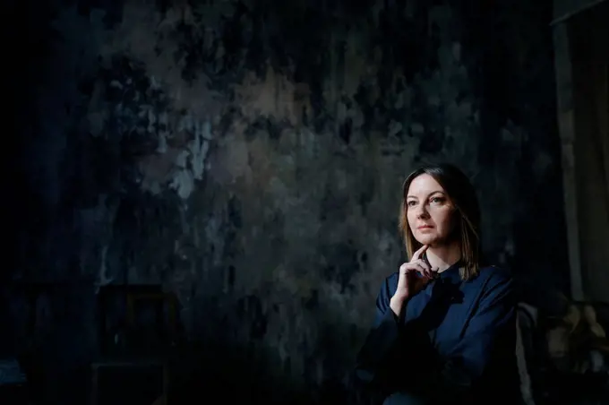 Thoughtful woman sitting with hand on chin against wall