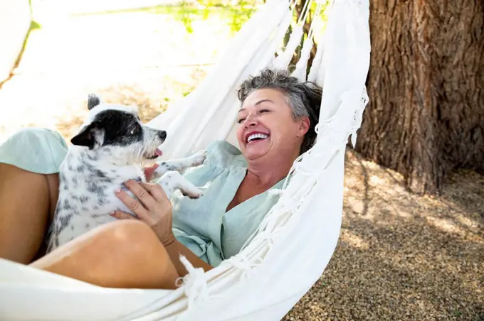 Happy woman with pet dog lying in hammock