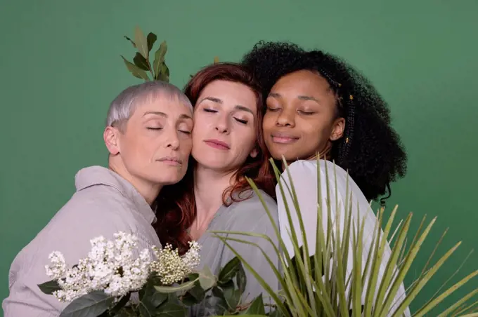 Multiracial friends with eyes closed standing against green background