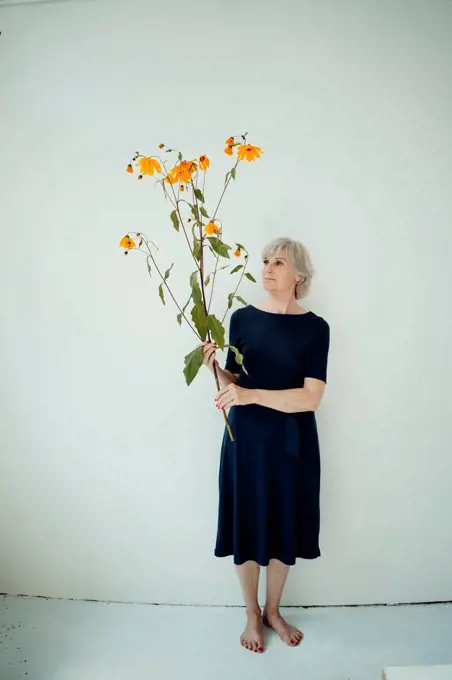 Senior senior woman with twig standing in front of wall