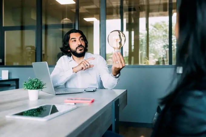 Businessman discussing over light bulb with colleague at work place