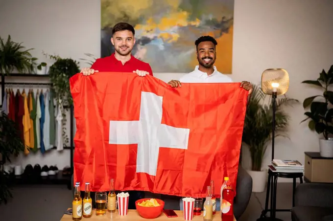 Happy football fans standing with Swiss flag at home