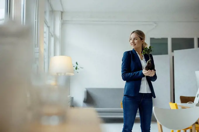 Smiling businesswoman holding plant in office