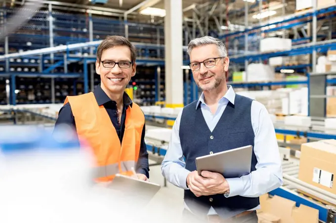 Happy worker standing by manager holding tablet PC in warehouse
