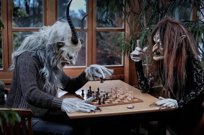 Mature man and woman in ghost costume playing chess game sitting at table