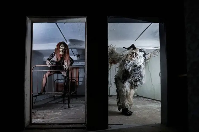 Man and woman in spooky costumes seen through door at horror house