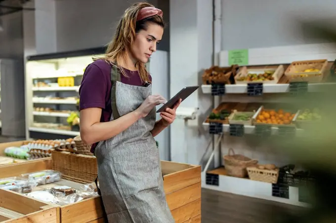 Store owner using tablet PC leaning on crate in organic market