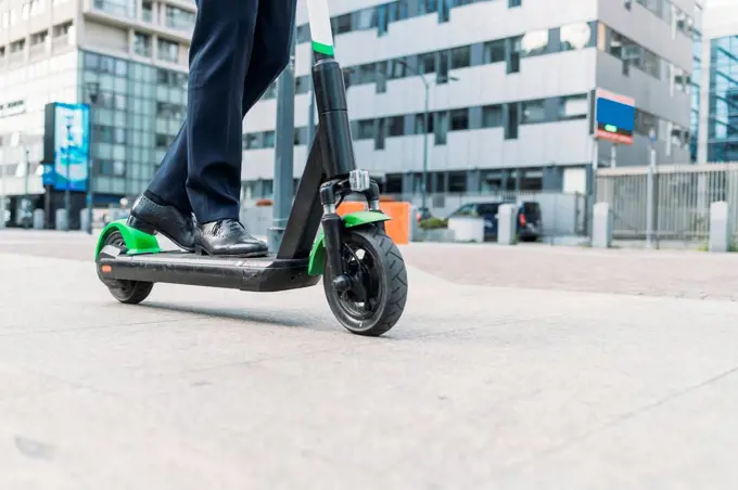 Businessman riding electric push scooter on footpath