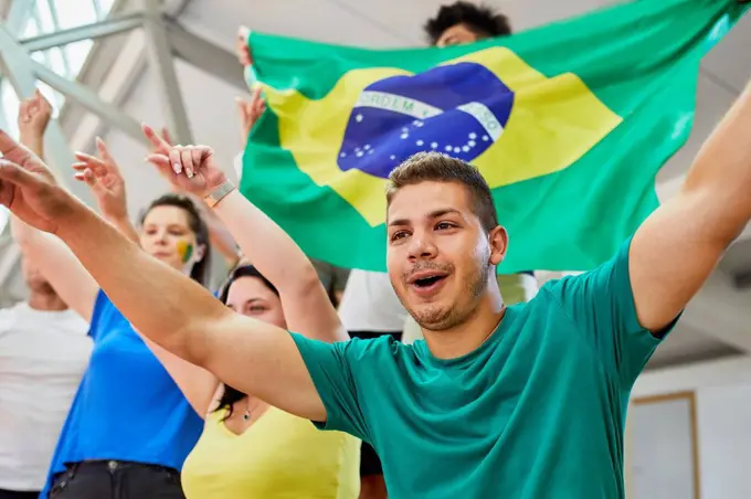 Man with arms raised cheering with fans at sports event in stadium