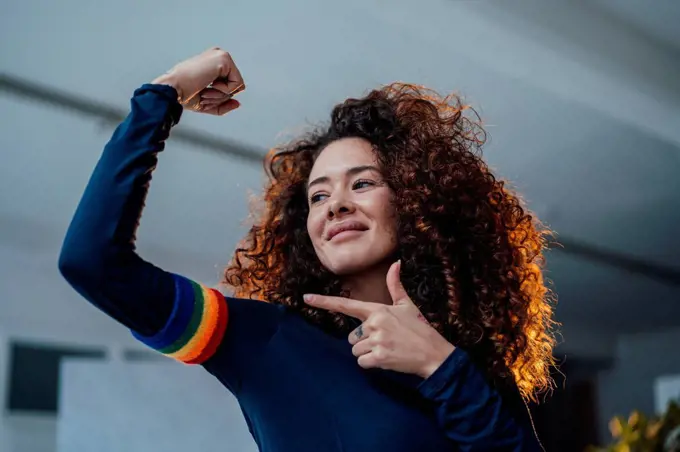 Smiling young woman flexing muscles pointing at rainbow arm band