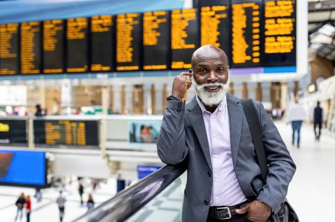 Smiling senior commuter with beard leaning on railing at railroad station