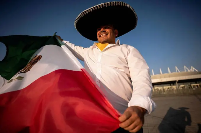 Smiling man wearing sombrero holding Mexican flag on sunny day