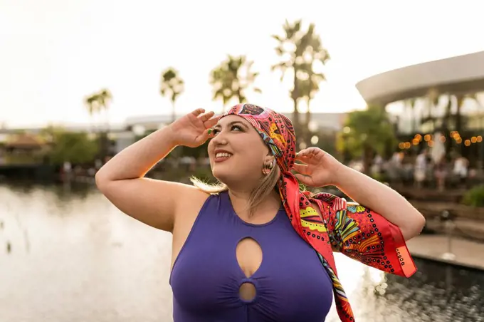 Happy young woman wearing colorful headscarf in front of lake