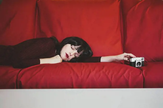 Woman with analog camera relaxing on red couch
