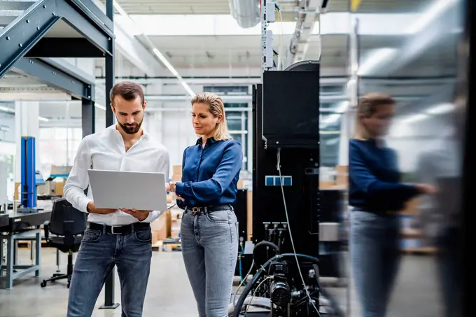 Business colleagues working on laptop standing in factory