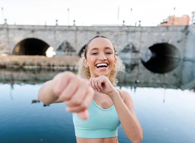 Happy sportswoman exercising and punching in front of lake