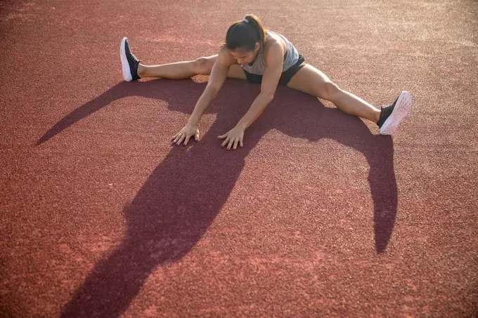 Young woman doing stretching exercise in sports field