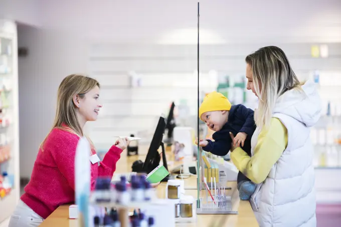 Happy pharmacist with customer holding son and buying medicine at pharmacy