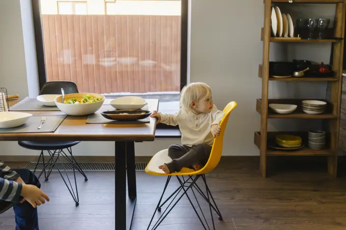 Blond girl sitting on yellow chair near dining table at home