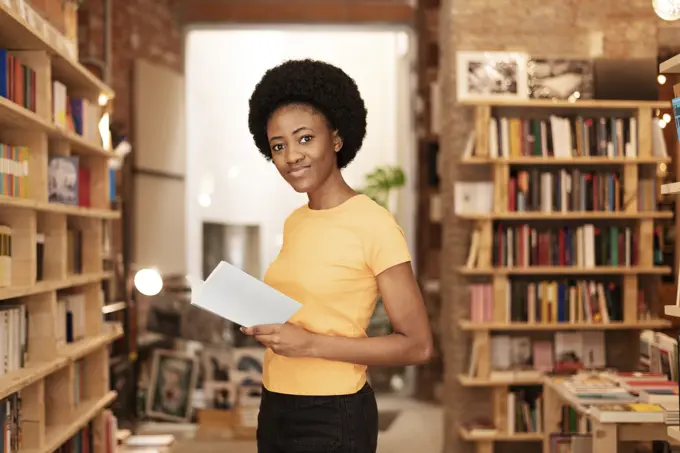 Smiling Afro woman holding book at library