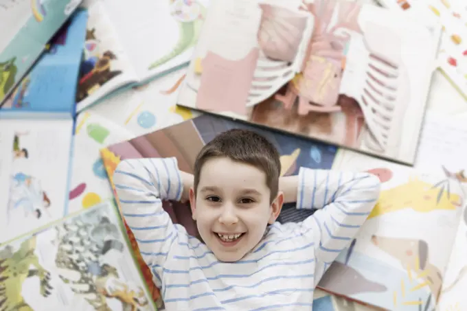 Smiling boy lying on floor amidst books at home