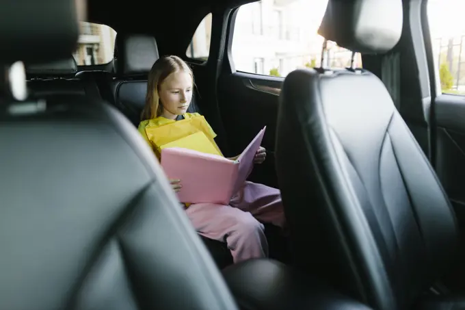 Focused girl reading book in backseat of car