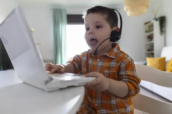 Boy wearing headset and using laptop at table