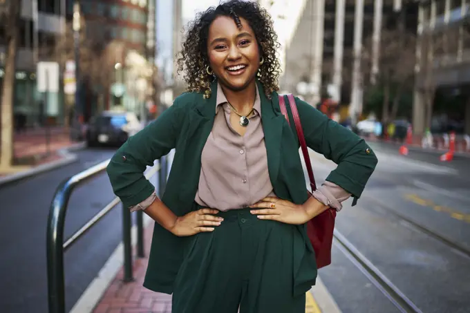 Happy young beautiful businesswoman with arms akimbo standing on street