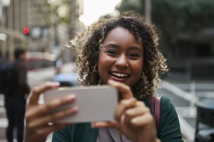 Smiling beautiful young businesswoman photographing through mobile phone